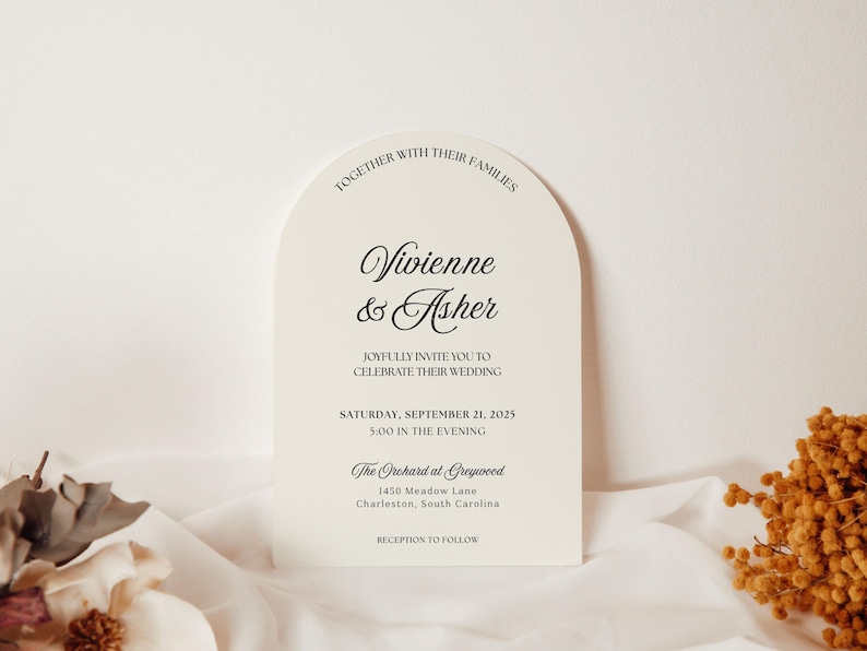 May include: An ivory wedding invitation with an arched top, featuring the names "Vivienne & Asher" in elegant script. The invitation includes the wedding date, time, and venue details. Dried floral accents are visible.