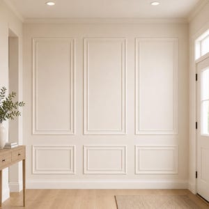 May include: A light beige hallway featuring a wooden console table with a white vase, green foliage, and a bowl. An arched mirror hangs above the table. The wall has white rectangular moulding panels, and a woven rug sits on the light wood floor.