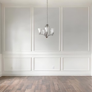May include: A white room with white wainscoting and a chandelier hanging from the ceiling. The floor is made of dark wood.