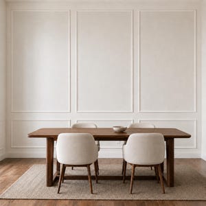 May include: A rectangular wooden dining table with four legs and a smooth surface, accompanied by two light beige upholstered chairs with wooden legs, positioned on a textured rug in front of a wall with white rectangular molding panels.