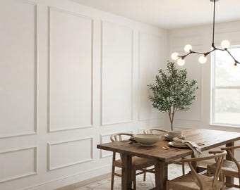 May include: A dining room featuring a wooden table with four chairs, a potted olive tree, and a modern branch chandelier with globe bulbs. The walls are white with rectangular molding panels, and a patterned rug covers the floor area.