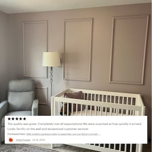 May include: A white crib with a white mattress and a pink pillow in a nursery with a light brown wall and white molding. The wall has three rectangular panels with white trim.