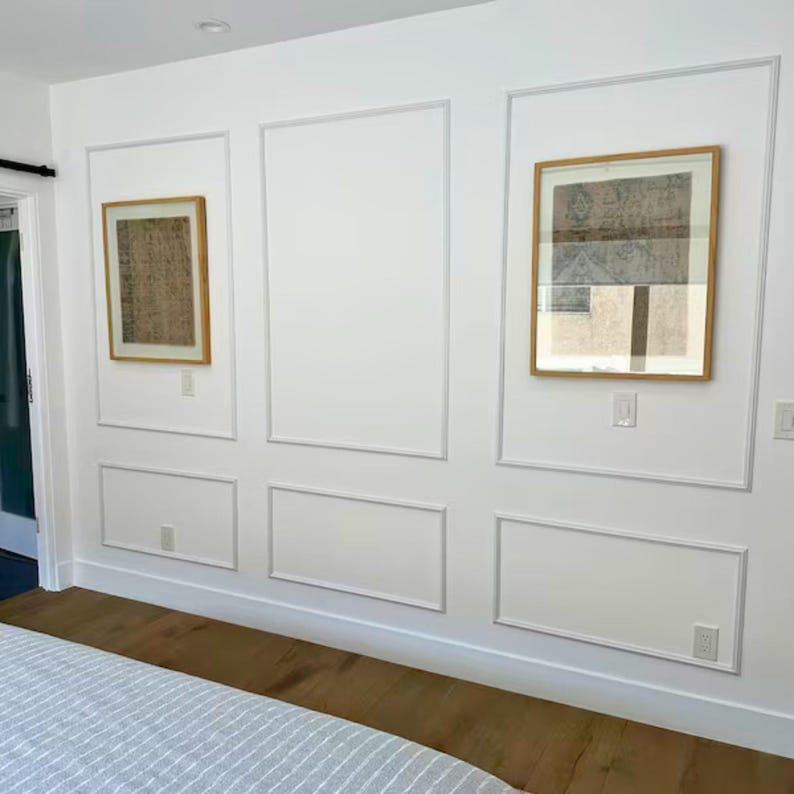 May include: Two framed artworks hang on a white wall with decorative molding. The artwork on the left has a tan background with dark brown markings. The artwork on the right has a brown and gray abstract design. The wall has a wood floor.