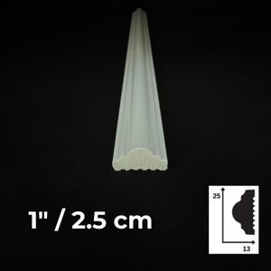 Puede incluir: Una moldura blanca alargada con un perfil decorativo curvo. La vista del extremo muestra un material texturizado y poroso. El texto en la imagen dice 1" / 2,5 cm, acompa&ntilde;ado de un diagrama que muestra dimensiones de 25 y 13 para el perfil.