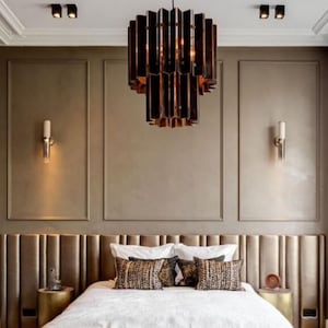 Könnte beinhalten: Ein Schlafzimmer mit einem großen Bett mit einer weißen Bettdecke und gemusterten Kissen. Das Kopfteil ist mit einem hellbraunen Stoff bezogen. Ein Kronleuchter hängt von der Decke und zwei Wandleuchten befinden sich an beiden Seiten des Bettes.