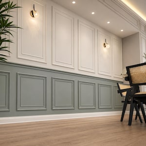 May include: A wall featuring two-tone wainscoting with a sage green lower section and an off-white upper section, both adorned with rectangular molding panels. Two black wall sconces with spherical glass shades are mounted on the upper wall.
