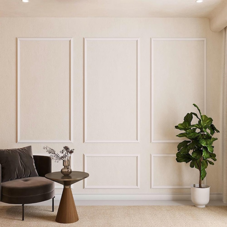 May include: A brown velvet armchair with a single pillow sits next to a small round side table with a vase of dried flowers. A potted ficus tree stands in the corner of the room. The walls are white with decorative molding.