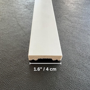 May include: A white, rectangular piece of wood trim, 1.6 inches (4 cm) wide, with a textured bottom edge. The trim is shown against a dark gray background.