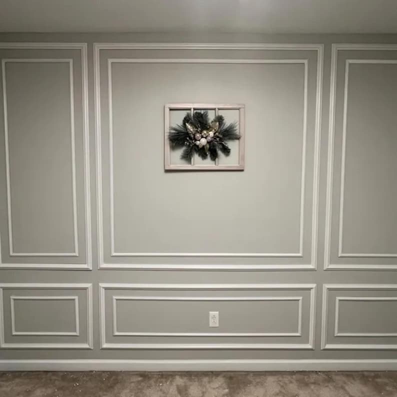 May include: A rectangular wooden window frame wall decoration featuring a central arrangement of dark green pine needles, silver-toned foliage, and a cluster of white and metallic gold spherical ornaments mounted on a light gray wall with molding.