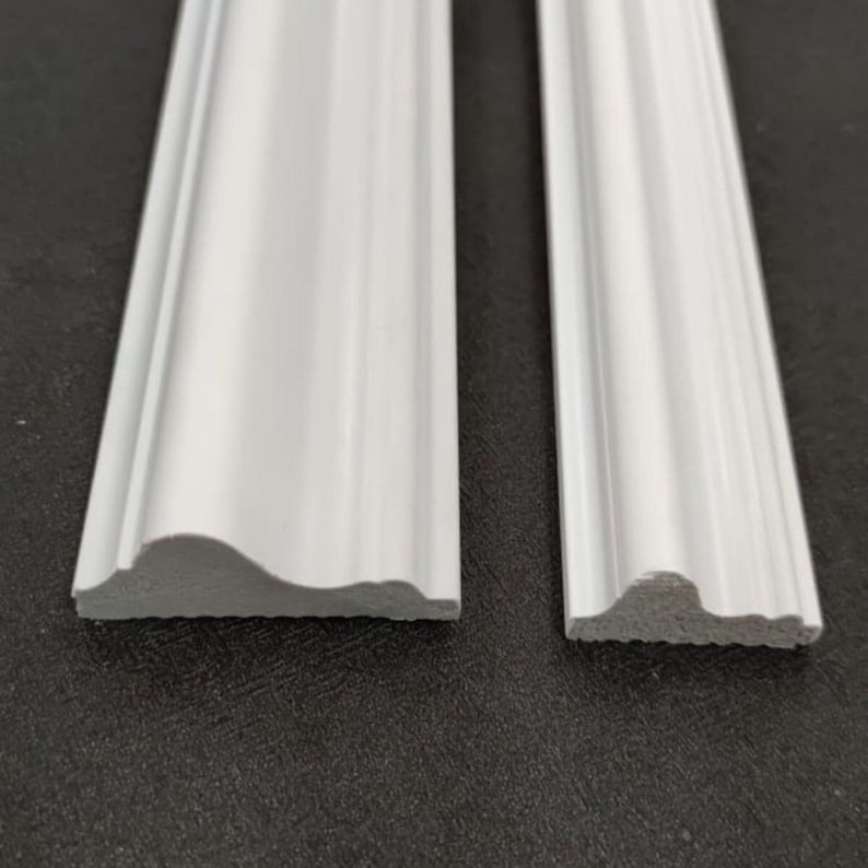 May include: Two pieces of white molding with a curved, decorative profile. Each piece features a smooth, rounded top edge that transitions into a series of subtle ridges and grooves, showcasing a clean, finished look for architectural trim.