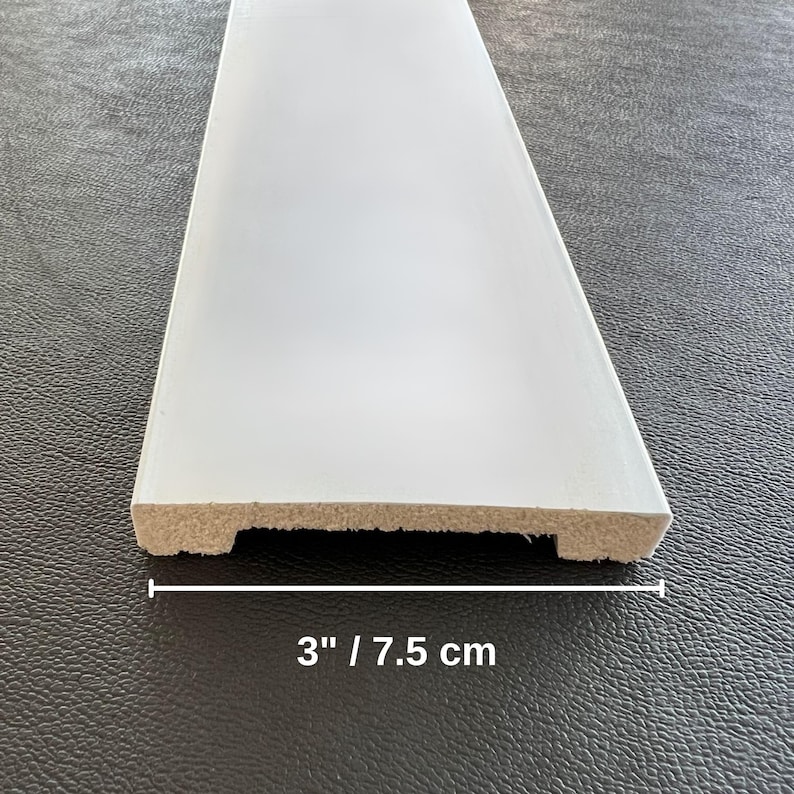 May include: A white painted wooden trim piece, 3 inches wide, with a beveled edge. The text "3" / 7.5 cm" is printed in black below the trim. The trim is likely for home improvement or woodworking projects.