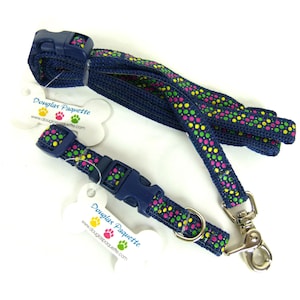 May include: A blue dog collar and leash set with a colorful paw print pattern. The collar and leash are made of durable nylon and feature a sturdy metal clasp. The set is packaged with a white tag that says "Douglas Paquette" and includes the website address.