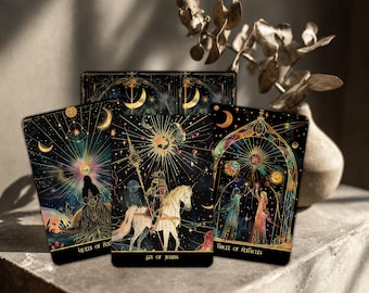 May include: A tarot card deck with a celestial theme. The cards feature illustrations with gold accents on a black background. The cards are arranged with three cards in the foreground, displaying the "Queen of Pentacles", "Six of Wands", and "Three of Pentacles".
