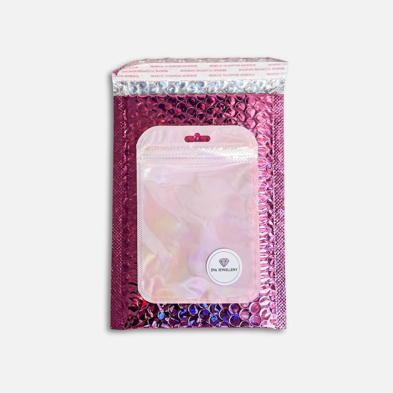 May include: A pink bubble mailer with a clear iridescent zip-top bag inside. The mailer has a metallic silver top and a peel-and-seal strip. The bag has a small white sticker with the text "EVA JEWELLERY".