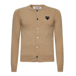 May include: A tan cardigan sweater with long sleeves and a button-up front. The sweater features a black heart-shaped logo with eyes on the left chest and the word "PLAY" above the top button.