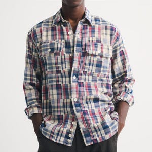 May include: A long-sleeve button-down shirt featuring a multi-coloured plaid pattern in shades of red, blue, and cream. The shirt includes a standard collar, a front button placket, and two chest pockets with buttoned flaps on each side of the front.