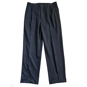 Könnte beinhalten: Eine dunkel anthrazitfarbene Hose mit Bundfalten, einem Hosenbund mit Gürtelschlaufen und umgeschlagenen Säumen. Die Hose hat einen geraden Schnitt mit einer sichtbaren Bügelfalte, die über die gesamte Länge jedes Hosenbeins verläuft.