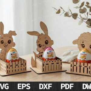 Può includere: Tre decorazioni pasquali in legno raffiguranti un coniglietto e un agnello, ciascuno con un ovetto Kinder Joy in una piccola recinzione. Il coniglietto e l'agnello sono marrone chiaro con dettagli intagliati. Le uova sono bianche, rosse e gialle.
