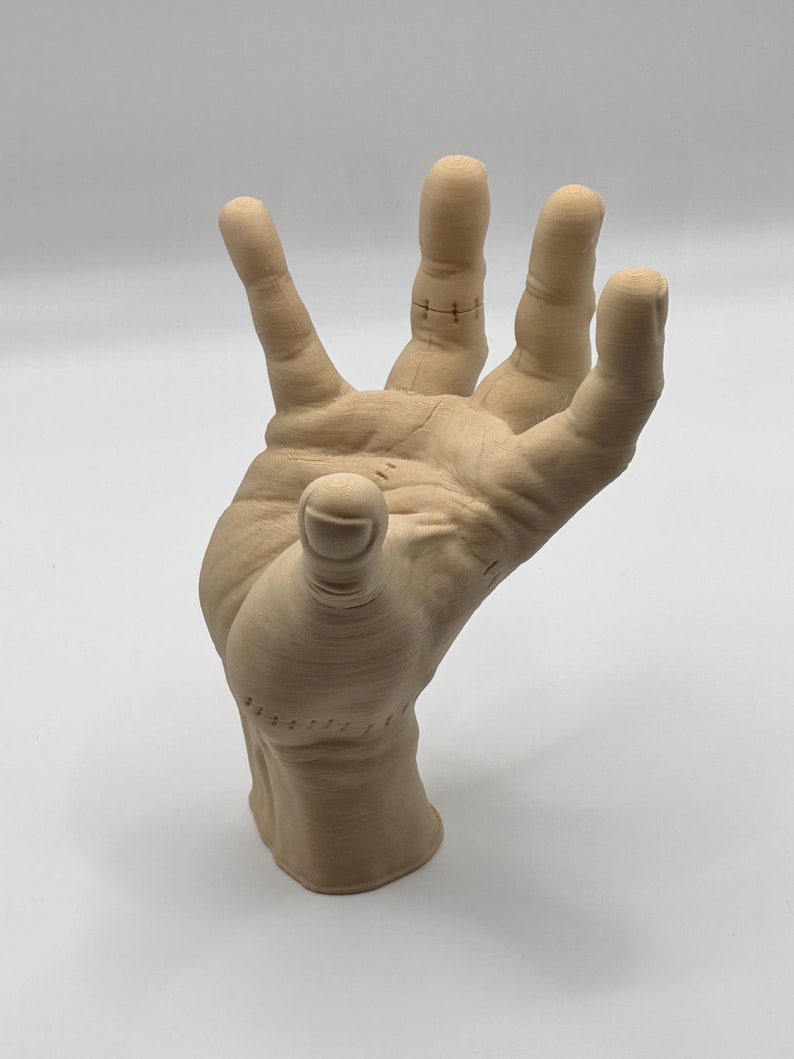 Puede incluir: Una escultura de mano de madera beige con detalles cosidos en los dedos. La mano est&aacute; levantada con los dedos extendidos.