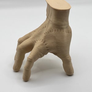 Puede incluir: Una mano beige impresa en 3D con costuras. La mano est&aacute; en posici&oacute;n con los dedos extendidos y ligeramente curvados.