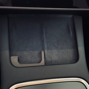 Op de afbeelding: Een zwart auto-interieur met een opbergvak met een uittrekbaar handvat.