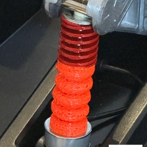 Könnte beinhalten: Nahaufnahme einer mechanischen Komponente mit einem roten, strukturierten, zylindrischen Element mit gestapelten Ringen, das an einer Metallstruktur befestigt ist. Das Bild enthält ein "Made in Germany"-Etikett.