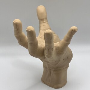 Puede incluir: Una escultura beige con forma de mano con texturas detalladas de los dedos y la palma. La escultura est&aacute; hecha de un material liso y mate y parece estar hecha de un tipo de resina.