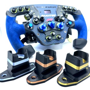 May include: Three 3D printed black plastic steering wheel mounts with gold, copper, and silver accents. Each mount has a V2.0 label and is designed to hold a steering wheel.