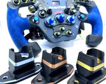 Puede incluir: Tres soportes para volante impresos en 3D de plástico negro con detalles dorados, cobrizos y plateados. Cada soporte tiene una etiqueta V2.0 y está diseñado para sujetar un volante.