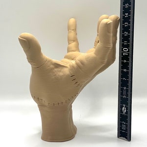 Puede incluir: Una mano beige impresa en 3D con costuras cosidas, que se muestra junto a una regla que mide 25,4 cm.