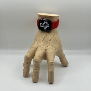 Puede incluir: Una banda de reloj Apple trenzada roja en una mano de maniqu&iacute;. La esfera del reloj muestra la hora 12:03.