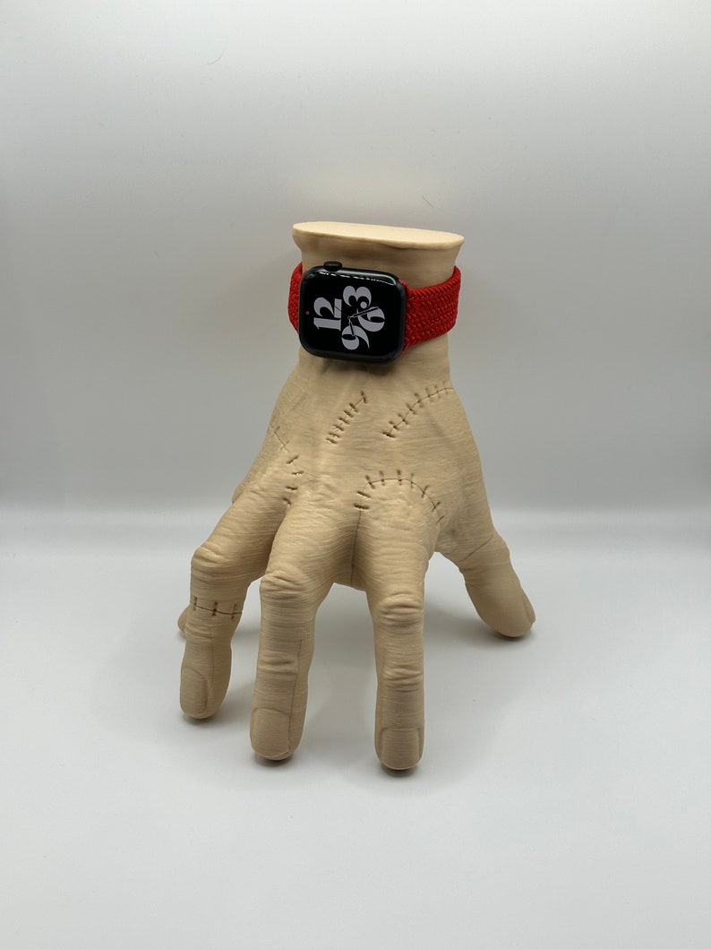 Puede incluir: Una banda de reloj Apple trenzada roja en una mano de maniqu&iacute;. La esfera del reloj muestra la hora 12:03.