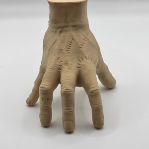 Puede incluir: Una mano esculpida de color beige con costuras cosidas en los dedos y la palma. La mano est&aacute; posada con los dedos extendidos y ligeramente curvados.