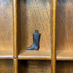 Puede incluir: Un organizador de cajones de madera con un pequeño amuleto de bota negra en uno de los compartimentos.
