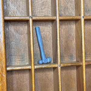 May include: A gray rubber mallet with a wooden handle, sitting in a wooden drawer.