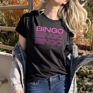 May include: A black t-shirt with the word "Bingo" repeated three times in pink lettering.