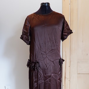 May include: A brown silk dress with a fringe trim. The dress has a round neckline and short sleeves.