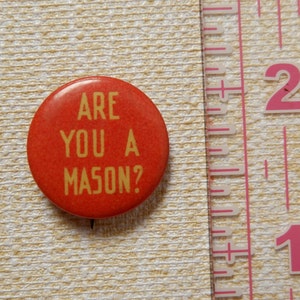 May include: A red button with the text "ARE YOU A MASON?" in yellow letters.