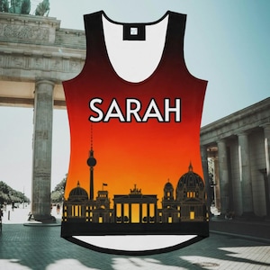 May include: A sleeveless vest top with a vibrant sunset design featuring the Berlin skyline. The name "SARAH" is printed in white block letters across the top. The top has a black and white trim.