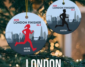 May include: Two blue and white round Christmas ornaments with a silhouette of a runner and the text "2025 London Finisher 26.2". One ornament has the name "Sadie" and the time "4:52:35" printed on it. The other ornament has the name "Austin" printed on it. The ornaments are hanging on a Christmas tree.
