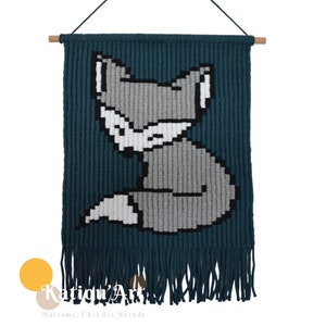 Può includere: Appeso a parete in macramè color verde acqua con un design di volpe grigia. La volpe è seduta con la coda arrotolata attorno al suo corpo. L'appeso a parete ha frange in basso.