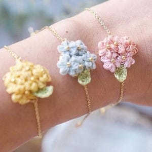 May include: Three delicate flower bracelets with gold chains. The flowers are crocheted and come in yellow, light blue, and pink.