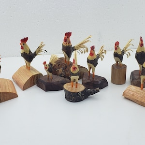 May include: A collection of eight hand-crafted wooden rooster figurines. Each rooster is painted with brown, black, yellow, and red accents. The roosters are displayed on various wooden bases.