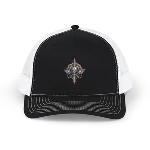 May include: A black and white trucker hat featuring a structured black front panel with a detailed embroidered emblem of a metallic skull, wings, and gear components. The cap includes a white mesh back, a curved black brim, and a button top.