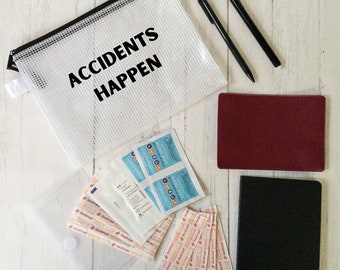 May include: A clear mesh zippered pouch with the text "ACCIDENTS HAPPEN" printed in black. The pouch is on a white wooden surface with a variety of first aid supplies, including bandages, antiseptic wipes, and two notebooks.