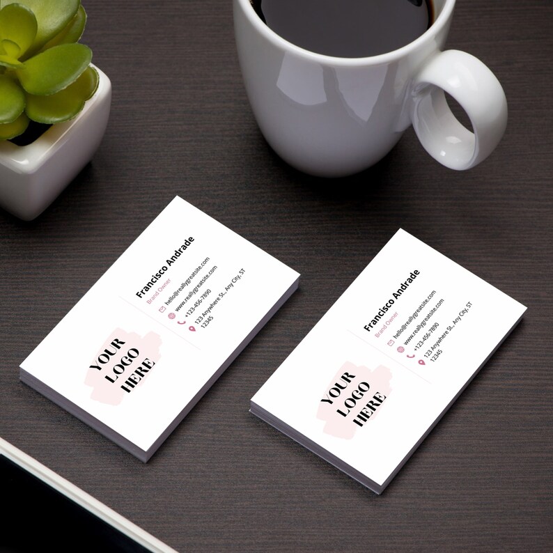 May include: Two white business cards with pink accents. The text on the cards reads "Francisco Andrade" and "Your Logo Here". The cards also include contact information, such as an email address, website, phone number, and address.