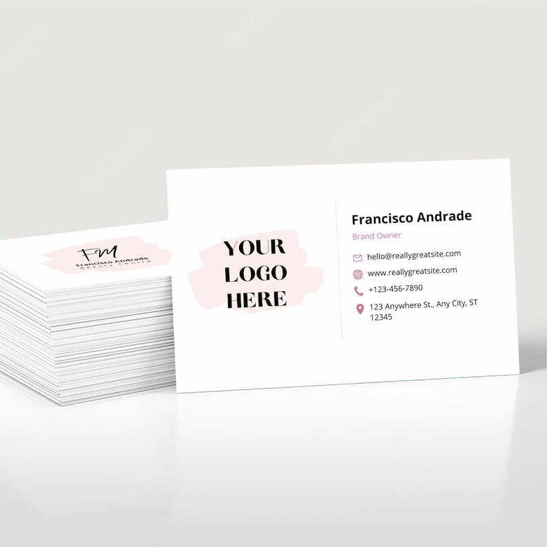 以下が含まれることがあります： ピンクと白のロゴと「YOUR LOGO HERE」というテキストが書かれた白い名刺の束。ブランドオーナーのフランシスコ・アンドラデの連絡先がロゴの下に記載されています。連絡先には、メールアドレス、ウェブサイトアドレス、電話番号、住所が含まれています。