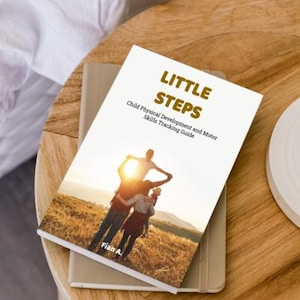 May include: A book titled "LITTLE STEPS" on a wooden table. The cover shows a family embracing in a field at sunset. The subtitle reads "Child Physical Development and Motor Skills Tracking Guide". The book is resting on a beige notebook.