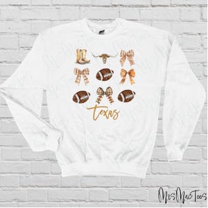 May include: White sweatshirt with a brown and white football, a brown and white bow, a brown and white steer head, and the word "Texas" in gold lettering.