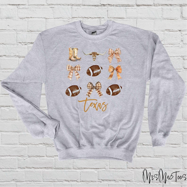 May include: A gray sweatshirt with a design featuring footballs, bows, boots, a longhorn steer, and the word "Texas".